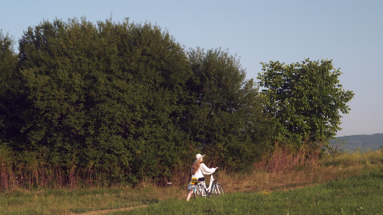 niña de vestido blanco empuja la bicicleta en el paisaje rural en la hora dorada en cámara lenta