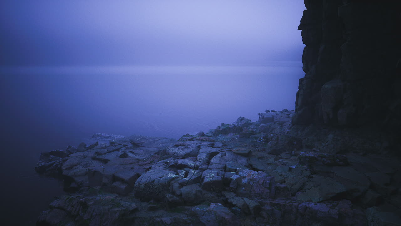 rocas costeras brumosas al amanecer con luz suave que se refleja en el agua