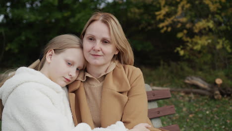 mom and daughter are sitting on a bench in the park on an autumn day