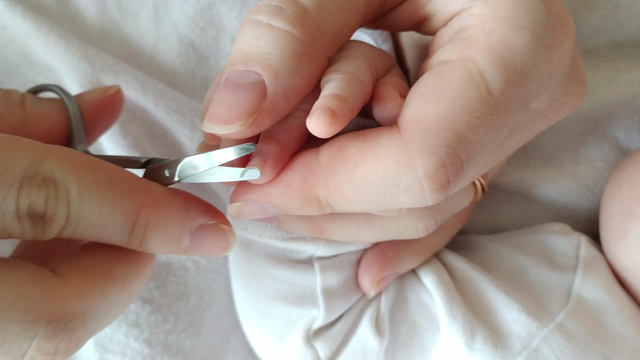 cortando las uñas de los bebés recién nacidos en la cama, las manos de la madre del padre usando tijeras para cortar las uñas de los dedos del hijo, vista superior de mano, interior, día