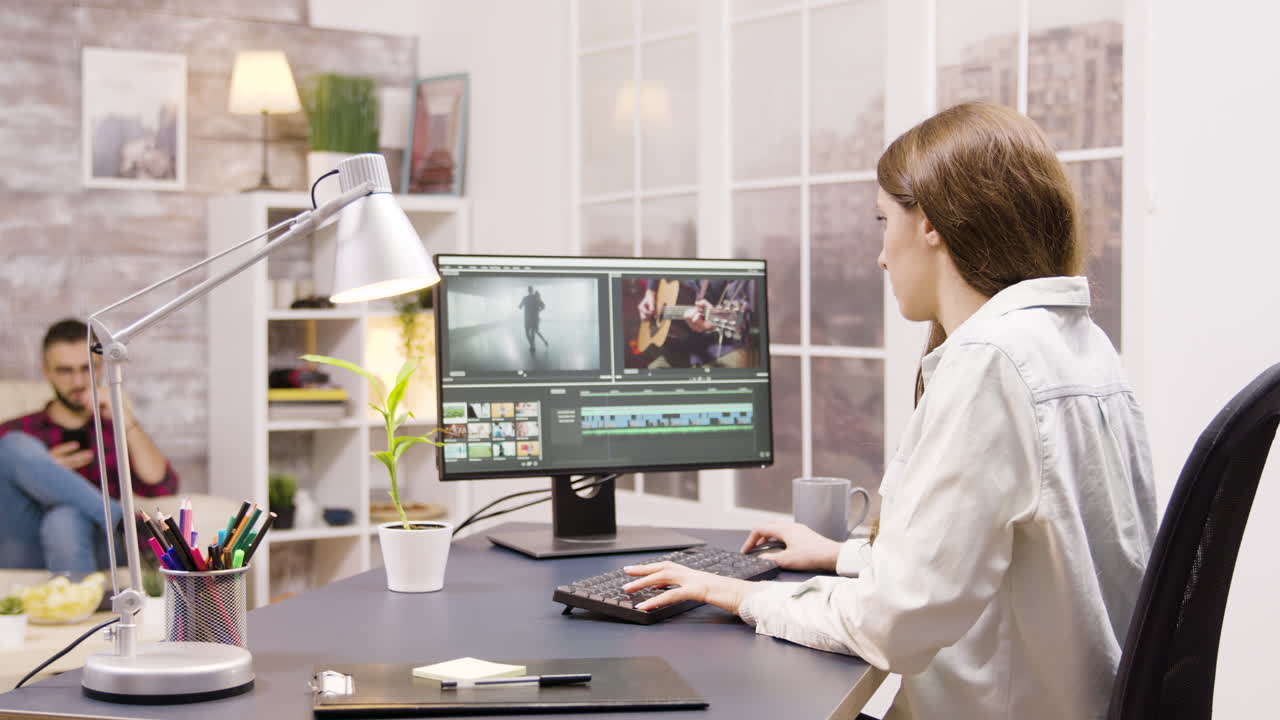 Woman editing video in her home office while man talks on the phone