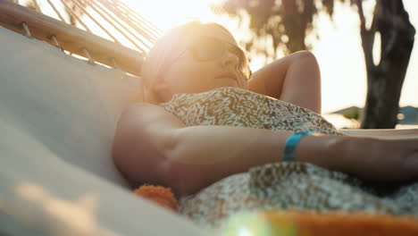 Una-Mujer-Turista-En-Un-Vestido-De-Verano-Se-Relaja-En-Una-Hamaca,-El-Sol-En-El-Horizonte-Crea-Hermosas-Altas