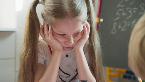 Girl-in-bad-mood-leans-face-on-hands-sitting-with-brother