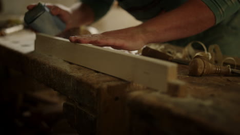 Man-checking-wood-softness-in-studio.-Unknown-guy-using-sandpaper-in-carpentry