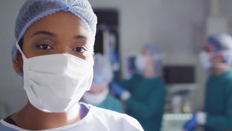 video portrait of african american female surgeon in face mask in operating theatre, with copy space