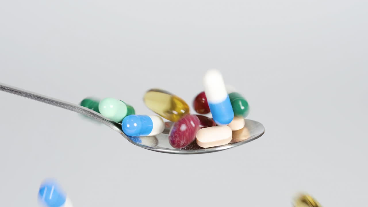 Tesoros nutricionales: cápsulas y píldoras multicolores de vitaminas y suplementos cayendo en una cuchara de metal. Medicamentos vibrantes que simbolizan la medicina moderna, el cuidado de la salud, el bienestar y diversos tratamientos.