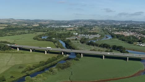 Antena-De-Tráfico-En-Movimiento-En-Una-Carretera-Muy-Transitada-Elevada-Sobre-Un-Campo-Verde-Prístino