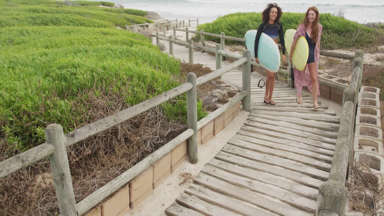 Grupo diverso de amigas felices que regresan de la playa llevando tablas de surf