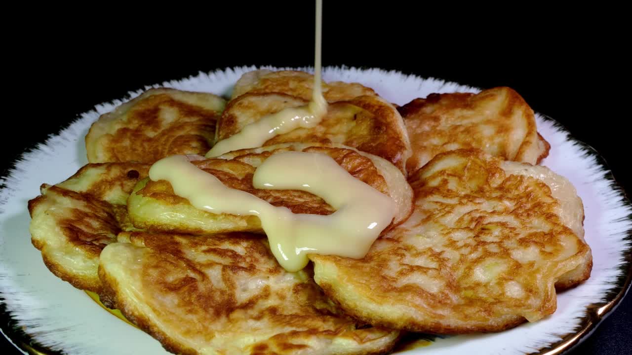 신선한 긴 집에서 만든 달한 팬케이크가 접시 위에 회전하고 응축 우유로 부어집니다.