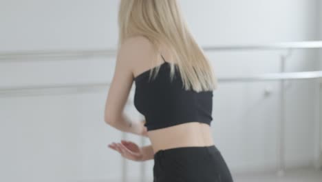 fit girl in black clothes performing contemporary. female dancer shows flowing motions, body and hands waves at white room. modern ballet dance choreography. young woman is moving smoothly