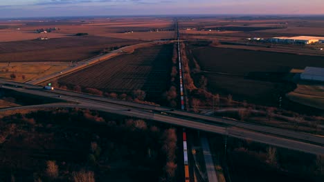 view of freight train traveling slowly under highway with traffic