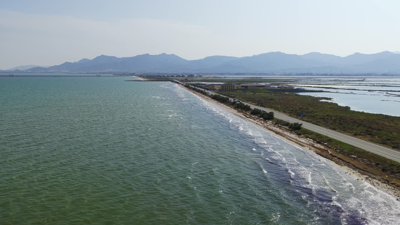 Cars driving along coastal road near salt evaporation ponds and the beach near Pula, Cagliari, Southern Sardinia, Italy