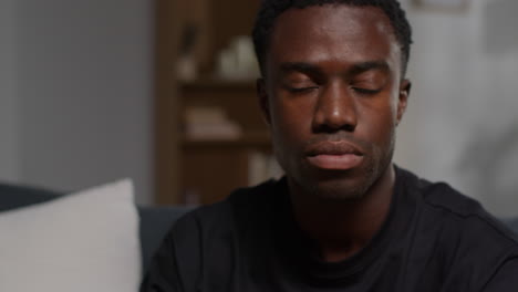 close up of unhappy and depressed young man sitting on sofa at home shaking head