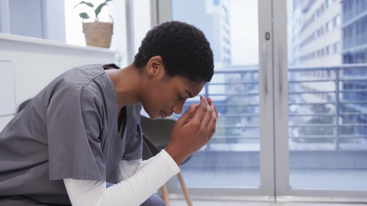 Tired african american female doctor sitting in hospital waiting room, slow motion
