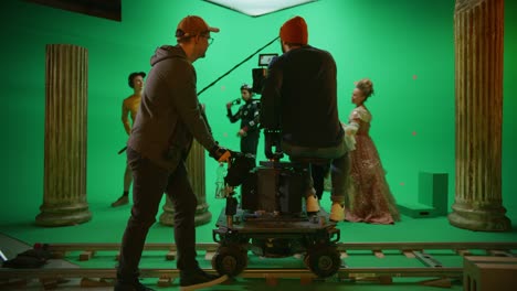 en el estudio de cine, el rodaje de la escena de la pantalla verde de la película de historia. el camarógrafo en movimiento en el tranvía del ferrocarril filma a dos actores disfrazados mientras el director controla el proceso. el equipo en la realización de películas de gran presupuesto