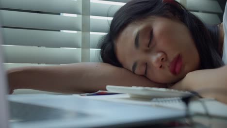 slow motion and close up of overworked and tired businesswoman asian sleeping on her desk and leaning on her arm at home office.modern problems and issues with working from home.