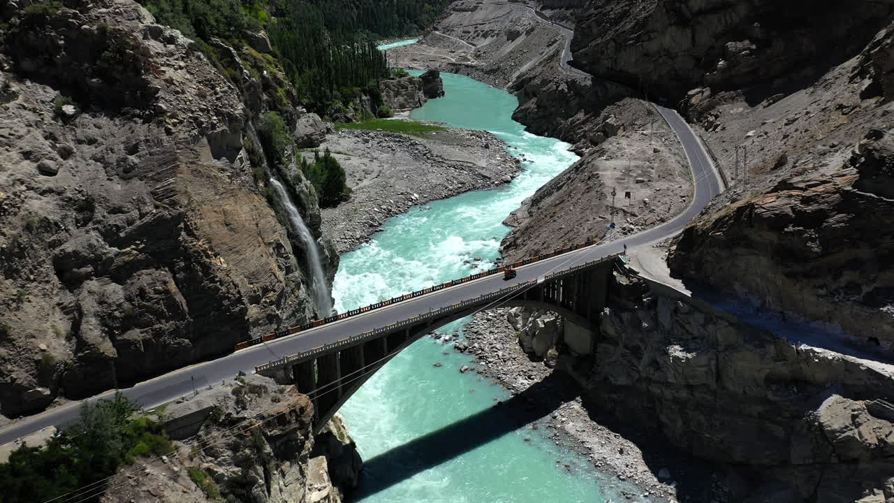 toma de drones del río de agua azul turquesa que fluye bajo un puente en la cordillera de karakoram a lo largo de la carretera de karakoram, revelando