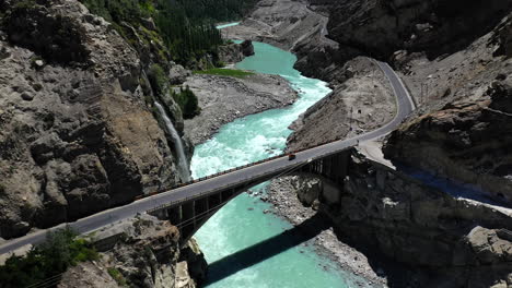 drone shot of turquoise blue water river flowing under a bridge in karakoram mountain range along karakoram highway, revealing