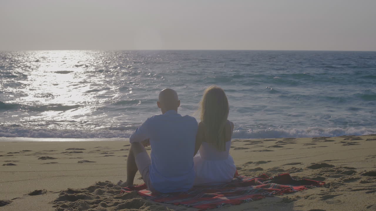 해변 에서 플레이드 에 앉아 있는 부부 의 뒷면