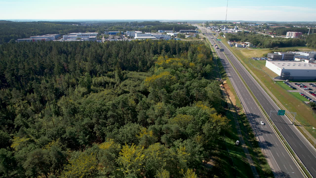 vuelo elevado del avión no tripulado sobre árboles verdes, autopista y almacén lejano