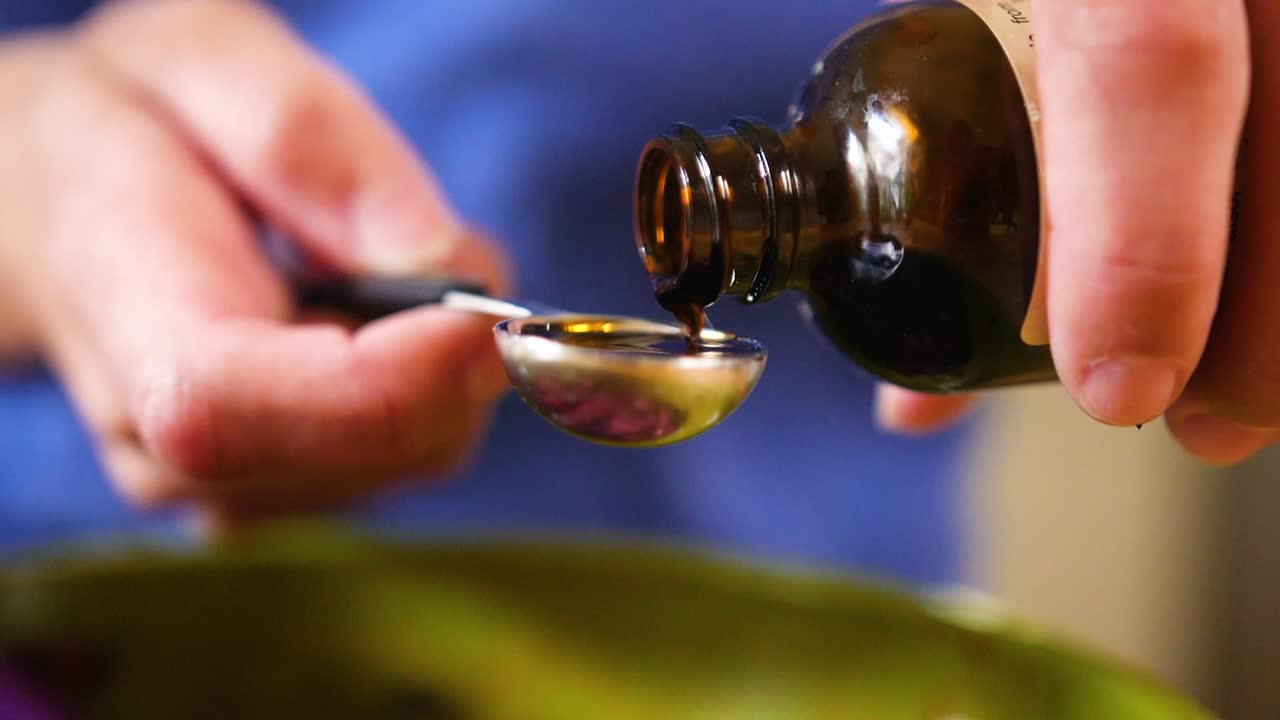 chiuda in su movimento lento versando l'estratto di vaniglia nel cucchiaio da tavola per cuocere una torta