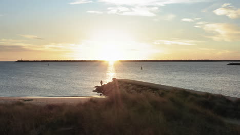 Sunset-shrouding-the-scenery-around-stone-pier-in-Praia-do-Cabedelo,-Viana-do-Castelo---Aerial-Wide-low-angle-slide-shot