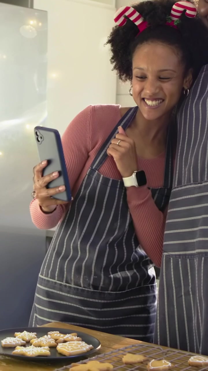 Vertical video: Bringing phone, woman and partner in aprons checking cookie picture in home kitchen