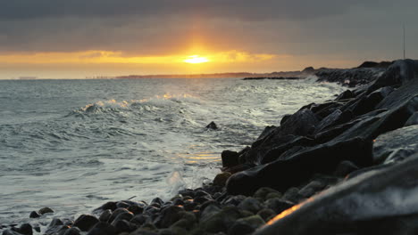 Stunning-sunset,-with-waves-gently-breaking-against-a-rugged-stone-dike-in-Denmark's-northernmost-region