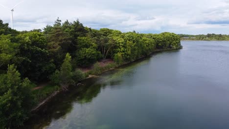 aerial above scenic landscape with a lake and trees in near breda, the netherlands. windturbine and clouds in the distant horizon.