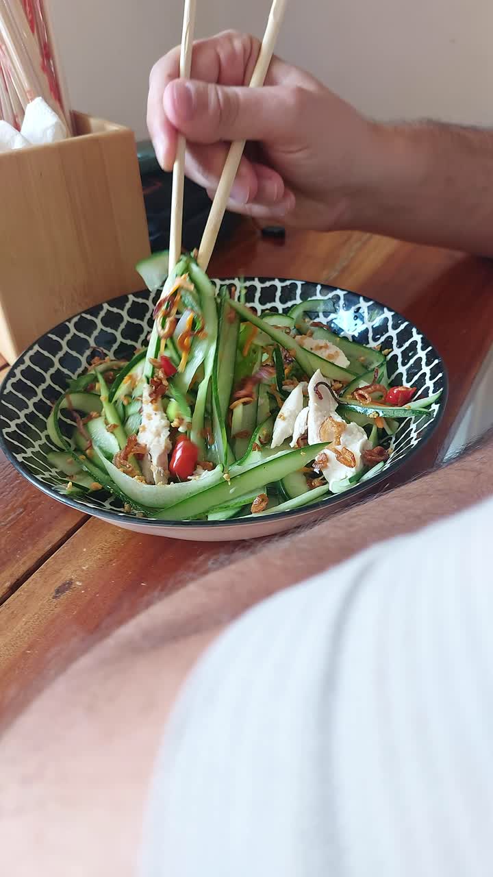 Overhead candid scene of using chopsticks to eat thit ga goi tom or Vietnamese chicken cucumber salad, authentic local dish from Vietnam