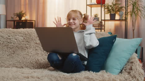young teenager girl laptop video call online chat at home sofa wave silly laughs funny faces energy