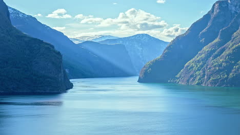 time lapse shot of flying white clouds between norwegian mountains and cruise ship leaving fjord during sunny day