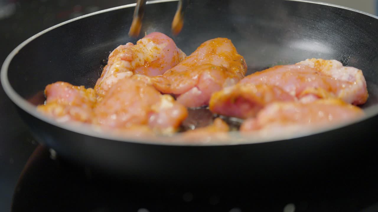 Primo piano di cosce di pollo crude marinate che iniziano a cuocere in una padella nera