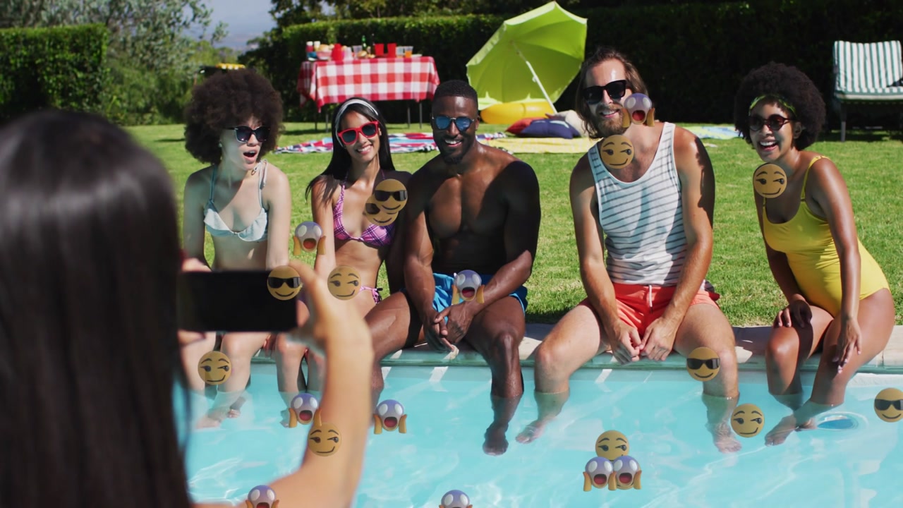 Woman holding phone and framing group at pool, sparking emojis rising with group waving for content