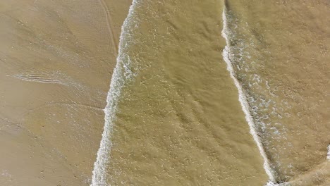 aerial footage of waves gently breaking on the beach, with golden sand