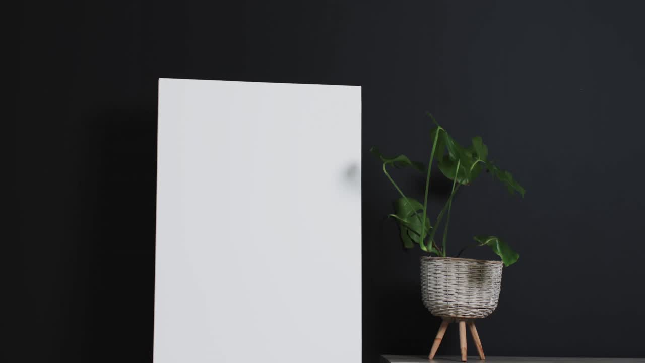video de un letrero de lienzo blanco en un caballete de madera con espacio de copia y planta en el escritorio sobre un fondo negro