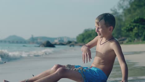 Preteen-Junge-In-Blauen-Shorts-Spielt-Mit-Sand-Auf-Der-Surflinie