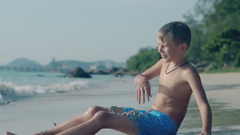 preteen boy in blue shorts plays with sand on surf line