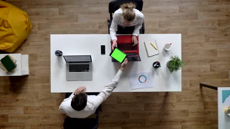 man giving tablet with chromakey to woman, topshot, sitting at table in modern office, work concept