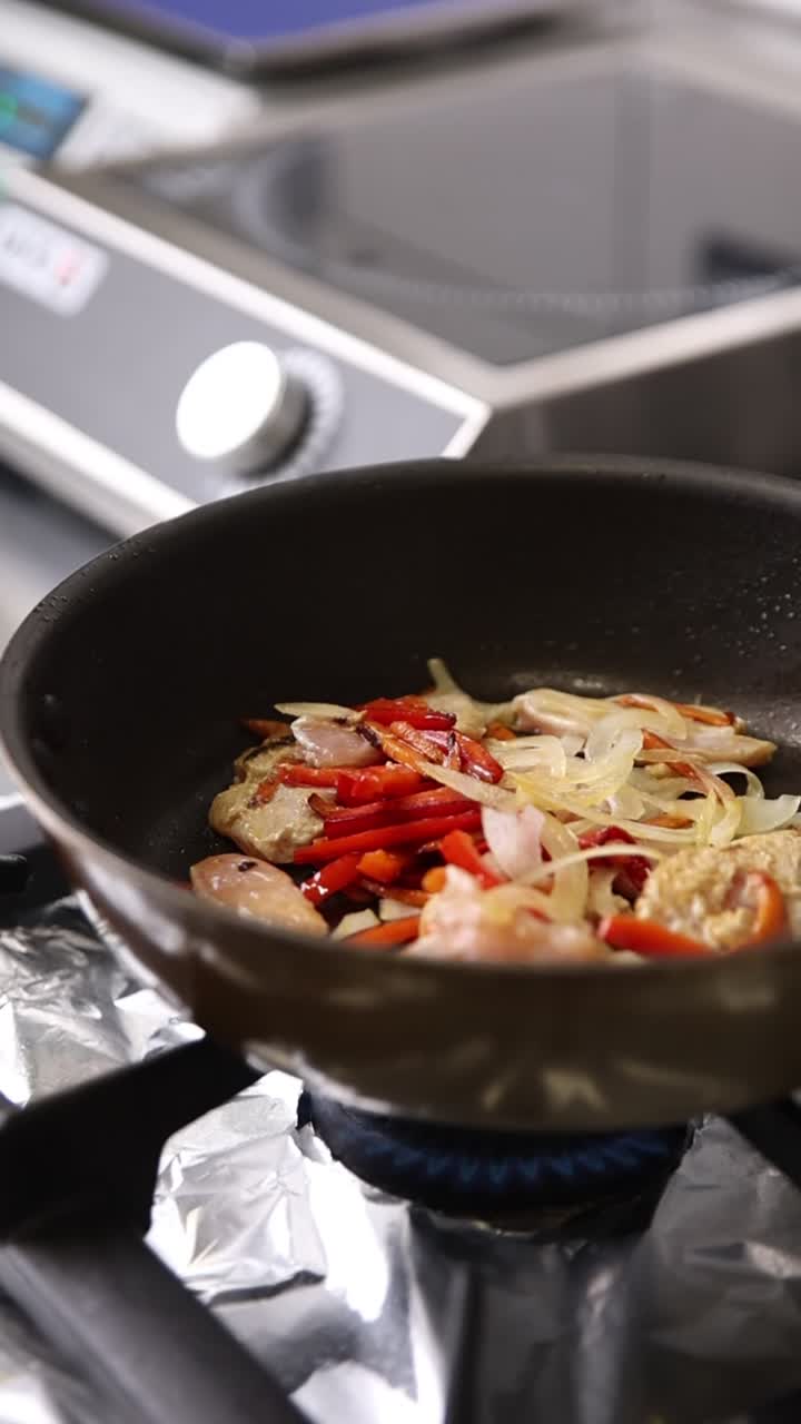 ガスコンロのフライパンで炒められる鶏肉と野菜。