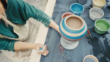 handmade crockery decoration. female potter carving pattern on painted handmade pot, top view, slow motion