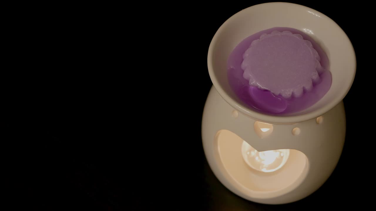 Vidéo en accéléré d'une cire de lavande violette fondante sur un brûleur de cire/huile en céramique blanche posé sur une table noire