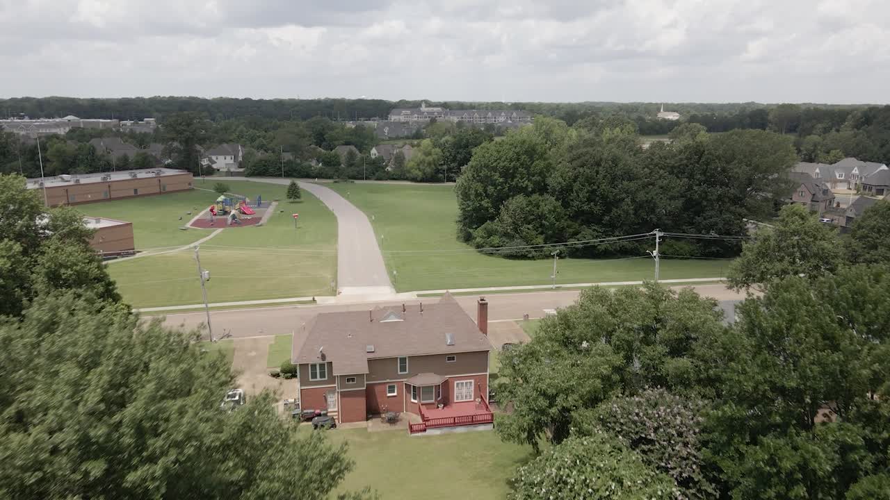 A drone zoom-in shot capturing a suburban neighborhood in the United States, showcasing tree-lined streets and residential houses. The greenery and -planned layout highlight the peaceful.