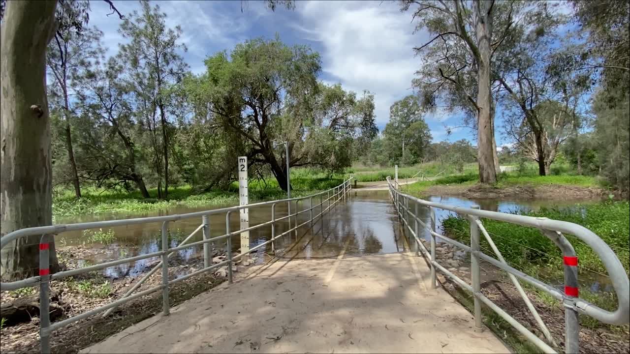 toma deslizante suave de derecha a izquierda de un puente peatonal inundado sobre un arroyo crecido después de la lluvia torrencial y la inundación en las inundaciones australianas en octubre de 2023