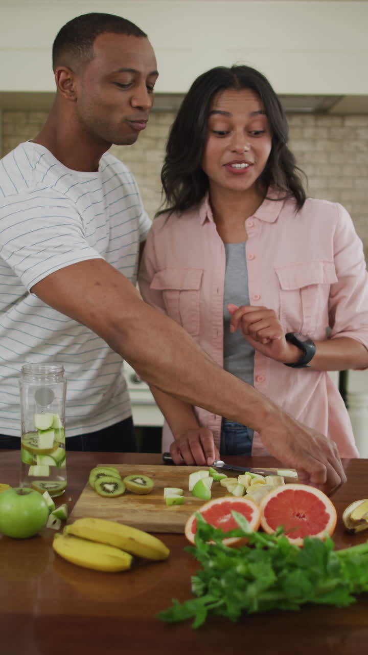 video vertical de una pareja feliz y diversa preparando comida juntos y comiendo en la cocina