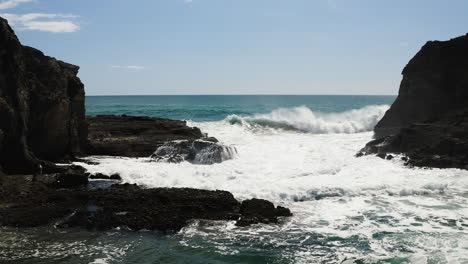 Looking-towards-the-sea-from-sandy-beach-as-foamy-water-rushes-into-narrow-cove