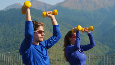 pareja haciendo ejercicio con pesas en las montañas