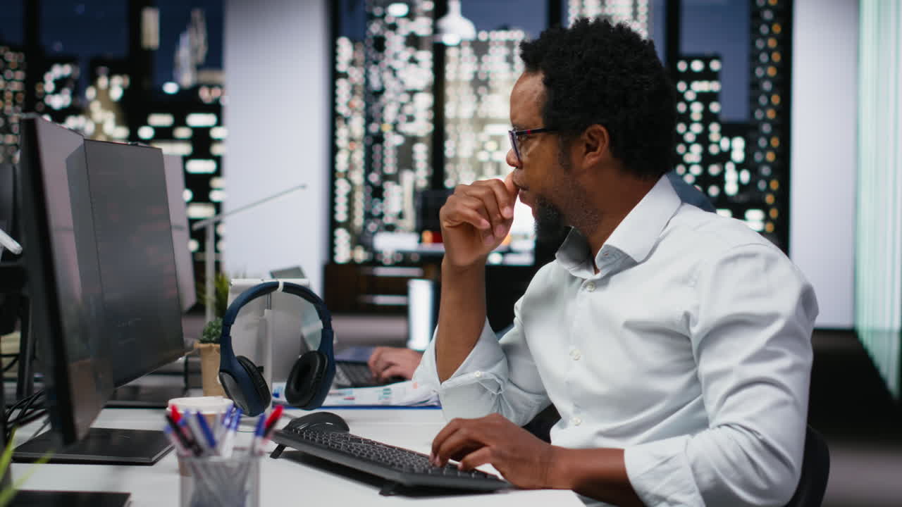 African American Programmer Working on Multiple Monitors in Modern Office at Night