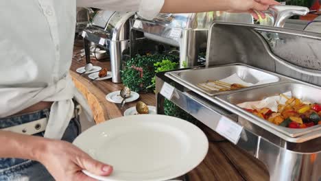 mujer que se sirve pollo griego con verduras en un buffet