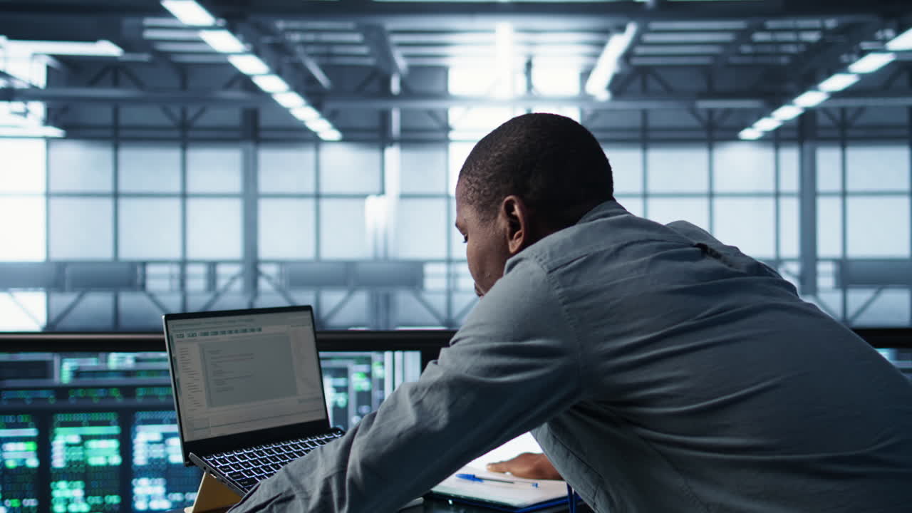 Technician coding on laptop in data center, managing server virtualization